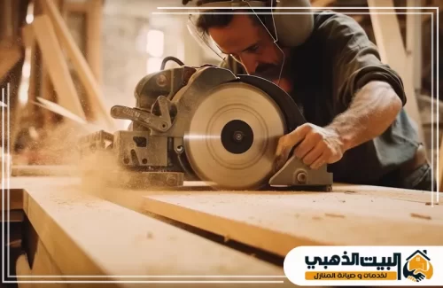 يظهر في الكادر نجار متمرس يقوم بدفع لوح خشبي طويل عبر منشار الطاولة الكهربائي