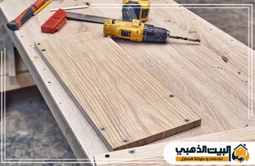 صورة علوية توضح مرحلة التجهيز على طاولة العمل، حيث يظهر مثقاب كهربائي (دريل) أصفر بجانب لوح خشبي